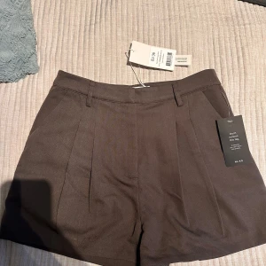 Bruna shorts med fickdetalj - Snygga bruna shorts med en stilren design och en diskret fickdetalj bak. Perfekta för en chic och avslappnad look. De har en klassisk passform och är tillverkade i ett bekvämt material.