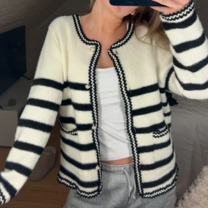 Randig kofta i svart och vit - Säljer en mysig randig kofta i svart och vit med knappar framtill. Koftan har långa ärmar och två fickor fram. Perfekt för en avslappnad stil.