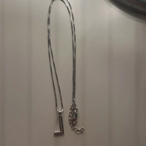 Silverfärgat halsband med bokstavsberlock - Elegant silverfärgat halsband med en enkel kedja och en bokstavsberlock. Perfekt för att ge en personlig touch till din stil.