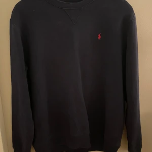 tröja från Polo Ralph Lauren - Snygg svart tröja från Polo Ralph Lauren med det klassiska röda logotypen på bröstet. Tröjan har en rund halsringning och långa ärmar, perfekt för en stilren look.