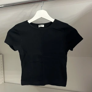 Svart ribbad topp från Kappahl - Säljer en stilren svart ribbad topp från Kappahl i storlek 146/152. Toppen har korta ärmar och en rund halsringning, perfekt för en enkel och snygg look.