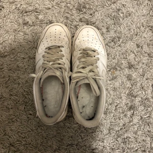 Vita Nike sneakers - Säljer ett par klassiska vita Nike sneakers med snörning. Perfekta för en avslappnad stil. Skorna har en robust sula och är i en tidlös design. Saknar sulor