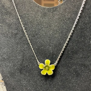 Blomformade smycken från Tomat - Set med halsband, örhängen och ring från Tomat. Alla smycken har en söt blomdesign i grönt och silver. Halsbandet har en enkel kedja med en blomma, örhängena är dinglande och ringen har flera små blommor och pärlor.