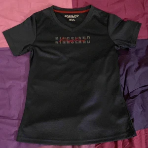 Svart t-shirt/ridtröja från Kingsland - Snygg svart t-shirt/ridtröja från Kingsland med korta ärmar och rund halsringning. Perfekt för en stilren look med diskret logga på bröstet. Tillverkad i ett bekvämt material som passar bra till vardags.