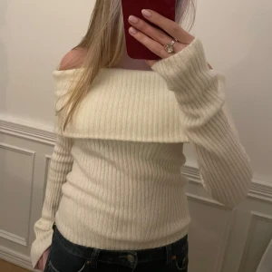 Stickad offshoulder-tröja - Säljer en stilren vit ribbad offshoulder-tröja med långa ärmar. Perfekt för en trendig look. Tröjan är oanvänd 