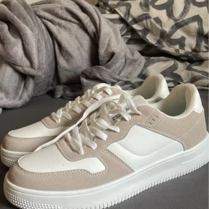 Beige och vita sneakers - Snygga sneakers i beige och vitt med snörning. Skorna har en stilren design med en kombination av syntet och mocka. Perfekta för en avslappnad stil.