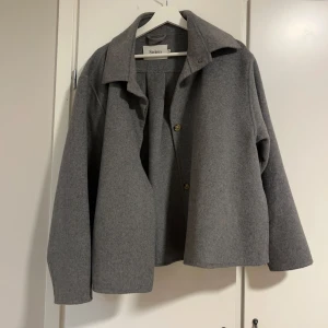 Grå kappa från Stylein  - Snygg grå kappa från Stylein med en stilren design. Jackan har en klassisk krage och knappar framtill. Perfekt för höst och vår, med en normal passform som ger en elegant look. Ordinarie pris-3900kr