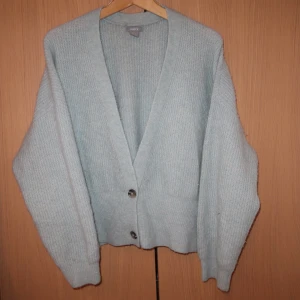 Ljusblå stickad kofta med knappar - Mysig ljusblå stickad kofta med djup v-ringning och knappar framtill. Perfekt för kyliga dagar och att mysa i. Koftan har långa ärmar och en avslappnad passform.