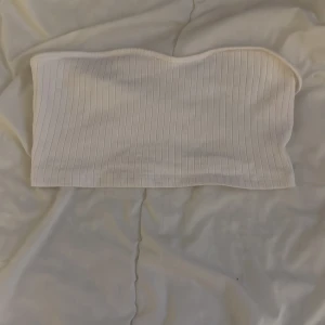 Vit ribbad tubtopp - Säljer en stilren vit ribbad tubtopp. Perfekt för sommardagar eller som ett basplagg i garderoben. Enkel och mångsidig design.