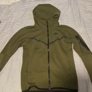 Grön Nike tech fleece  - Säljer en grön huvtröja från Nike med dragkedja och huva. Tröjan har långa ärmar och en ficka på ärmen. Perfekt för en sportig look. 