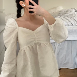Vit blus med puffärmar - Säljer en söt vit blus med puffiga långärmar och en v-ringad design. Blusen har ett subtilt mönster och en luftig passform som ger en romantisk känsla. Perfekt för att lyfta vilken outfit som helst! Från bikbok, köpt nångång 2023. Aldrig använd! 200kr