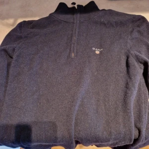 Mörkblå tröja med dragkedja från Gant - Säljer en stilren mörkblå tröja från Gant med halv dragkedja och broderad logga på bröstet. Perfekt för kyligare dagar med sin mjuka och bekväma passform. Lite mindre är vanlig M