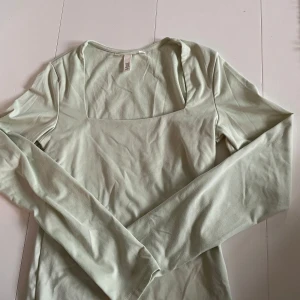 Ljusgrön långärmad topp från H&M - Säljer en stilren ljusgrön långärmad topp från H&M. Toppen har en fyrkantig halsringning och är tillverkad i ett mjukt material som ger en skön passform. Aldrig använd