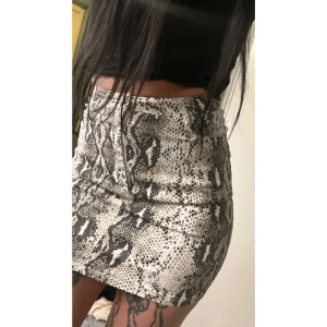 Ormmönstrad kortkjol, strl 34 - Snygg kortkjol med ormmönster i beige och svart. Den har en dragkedja framtill och två fickor bak. Storlek 34.