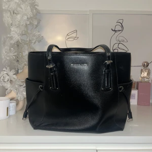 Svart axelväska från Michael Kors NK - Snygg svart axelväska från Michael Kors i skinn. Väskan har två handtag och flera praktiska fack på sidorna. Perfekt för att bära med sig allt man behöver. Stilren design med diskreta detaljer.KÖPT PÅ NK