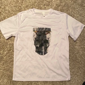 Vit t-shirt med dödskalletryck från Philipp Plein - Snygg vit t-shirt från Philipp Plein med ett stort dödskalletryck på framsidan. Perfekt för en cool och avslappnad stil.                                                                           Materialet påminner mer om en tränings tröja.                      Sitter större i storleken
