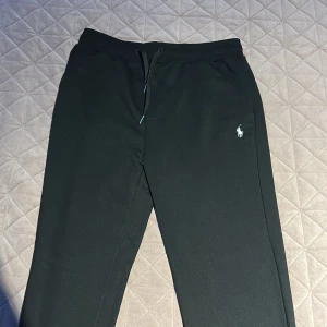 Svarta mjukisbyxor från Ralph Lauren - Snygga svarta mjukisbyxor från Ralph Lauren med dragsko i midjan och den klassiska loggan på benet. Perfekta för en avslappnad stil.