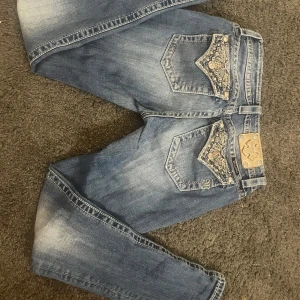 Blå jeans med broderade fickor från Miss Me - Snygga blå jeans från Miss Me med unika broderade detaljer på bakfickorna. Jeansen har en klassisk femficksdesign och en knappgylf. Perfekta för dig som vill ha något extra i garderoben.   (Kan gå ner i pris försöker bli av med dem snabbt)