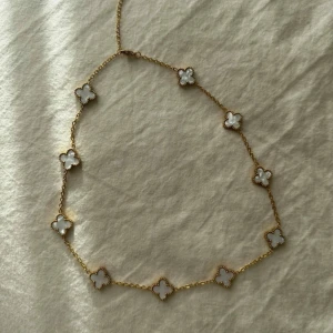 Guldhalsband med vita fyrklöver - Elegant guldhalsband med vita fyrklöverformade hängen. Vattentålig och aldrig använt. 