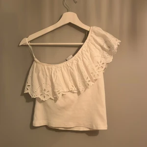 Vit offshoulder topp från Zara - Säljer en söt vit offshoulder topp från Zara med vacker spetsdetalj. Toppen har en volang, perfekt för varma dagar.  passar storlek 152. Perfekt för en somrig look! 🌸