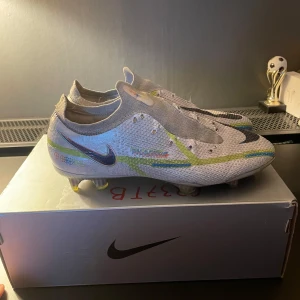 Nike phantom - Snygga Nike fotbollsskor i vitt med färgglada detaljer och en stor Nike-logga på sidan. Skorna har en modern design med snörning och är perfekta för fotbollsplanen. De har en lätt och smidig konstruktion för optimal prestanda.