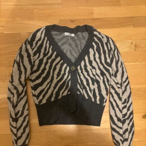 Zebramönstrad kofta från Dilvin - Snygg zebramönstrad kofta från Dilvin i grått och beige. Koftan har en v-ringad design med knappar framtill och långa ärmar. Perfekt för att ge din outfit en trendig touch 🖤