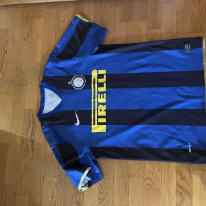 Zanetti fotbollströja - Säljer en klassisk blå och svart randig fotbollströja från Nike med korta ärmar. Tröjan har ett tryck av 'Pirelli' på framsidan och 'J. Zanetti 4' på baksidan. Perfekt för fotbollsfans!