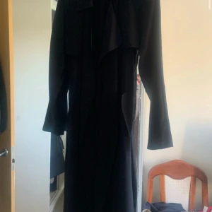 Svart trenchcoat med knyt XS - Snygg svart trenchcoat med knytband i midjan. Jackan har långa ärmar och en klassisk design som passar perfekt för höst och vår. Perfekt för att ge en stilren look. Från BikBok