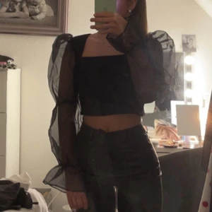 Svart topp med puffärmar - Trendig svart topp från ASOS med transparenta puffärmar i ett lätt och luftigt material. Toppen har en fyrkantig urringning och en lätt öppen rygg som knäps i nacken. Perfekt för att ge en elegant touch till din outfit.