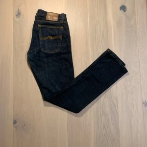 Nudie jeans ”tight long John” - Snygga mörkblå jeans från Nudie Jeans med klassisk femficksdesign och kontrastsömmar. Jeansen har en rak passform och är tillverkade i slitstarkt denim. Perfekta för en stilren look.
