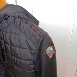 Svart parajumper  - Snygg svart quiltad jacka från parajumper  med dragkedja och huva. Jackan har långa ärmar och en broderad logga på ärmen. Perfekt för kyligare dagar med sin stilrena design och praktiska fickor. Kvitto finns me helt ny köpt 1 vecka sen 