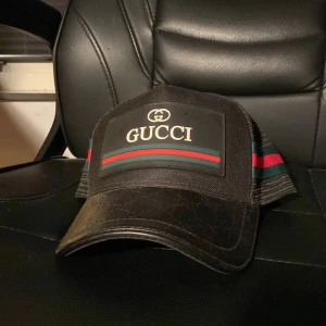 Svart keps från Gucci - Snygg svart keps från Gucci med klassiska ränder i rött och grönt. Kepsen har ett nätmaterial baktill och justerbar passform. Perfekt för en stilren look.