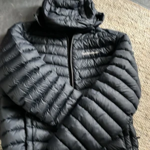 Svart dunjacka från Peak Performance - Säljer en svart dunjacka från Peak Performance. Jackan har en stilren design med dragkedja och är perfekt för kyligare väder. Den är quiltad för extra värme och komfort. Ett måste för garderoben!