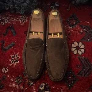 Bruna mockaloafers från Tiger of Sweden - Snygga bruna loafers i mocka från Tiger of Sweden. Perfekta för en stilren look. Skorna har en klassisk design med en bekväm passform. Aldrig använda, endast prövade.