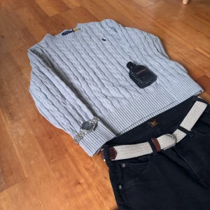 Grå stickad tröja från Ralph Lauren - Säljer en stilren grå stickad tröja från Ralph Lauren med kabelstickat mönster. Tröjan har långa ärmar och en rund halsringning. Perfekt för kyligare dagar och ger en klassisk look.