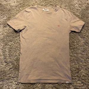 Beige t-shirt från Les Deux - Säljer en stilren beige t-shirt från Les Deux med korta ärmar och en liten broderad logga på bröstet. Perfekt för en avslappnad look.