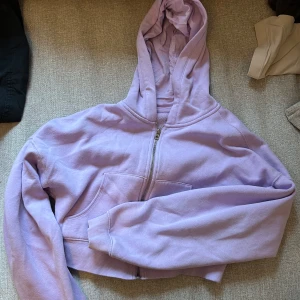 Lila croppad hoodie från H&M - Säljer en snygg lila hoodie från H&M med dragkedja och huva. Perfekt för en avslappnad stil. Den har långa ärmar och en bekväm passform.