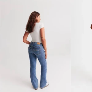 Blå jeans från Gina Tricot - Snygga y2k low bootcut mid blå, figurnära  jeans från Gina Tricot med klassisk femficksdesign och bälteshällor, framfickor och bakfickor med lock och knapp.De har är perfekta stretchiga  kvalitet jeans för en avslappnad stil. Lågmidjade med figurnära passform. Jeansen är blåa och har utsvängda ben med MÅTT: normallängd. Innerbenslängd 82cm i stl 38