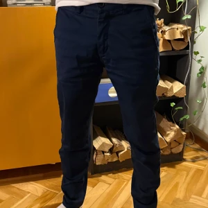 Mörkblå velour chinos - Snygga mörkblå chinos med snygg backtag och normal passform. Byxorna har en klassisk design med knappar och en diskret logga på baksidan. Perfekta för en stilren look.