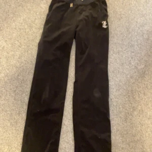 Svarta byxor från Juicy Couture - Snygga svarta byxor från Juicy Couture med glittrande logga på baksidan. Byxorna har en bekväm passform och är perfekta för en avslappnad stil. Tillverkade i mjukt material för extra komfort.