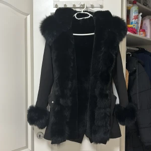 Svart pälsjacka med huva - Snygg svart jacka med pälsdetaljer på huva, ärmslut och framkant. Jackan har en elegant design med långa ärmar och en skön passform. Perfekt för kyliga dagar när du vill hålla stilen. 🖤pälsen på luvan går att ta av och storleksmässigt så passar den S/M