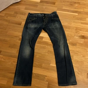 Blå jeans från Replay - Säljer ett par snygga blå jeans från Replay. De har en klassisk femficksdesign och en knappgylf. Perfekta för en avslappnad stil. Midja 44 cm, ben öppning 20 cm