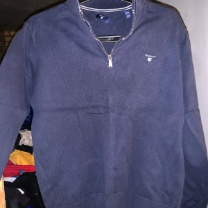 Mörkblå tröja med dragkedja från Gant - Säljer en stilren mörkblå tröja från Gant med dragkedja vid halsen. Tröjan har en diskret logga på bröstet och är perfekt för en avslappnad look. Passar bra till både jeans och chinos. Barnstorlek M/ motsvarande S i vuxen 