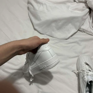 Vita Nike Air Force sneakers - Säljer ett par klassiska vita Nike Air Force sneakers. Skorna har en stilren design med snörning och är tillverkade i syntetmaterial. Perfekta för en casual look.