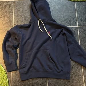 Mörkblå hoodie från Ralph Lauren - Säljer en snygg mörkblå hoodie från Ralph Lauren med det klassiska röda logotypen på bröstet. Hoodien har en känguruficka och vita dragsnören vid huvan. Perfekt för en avslappnad stil.