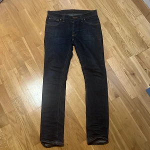 Mörkblå jeans från Nudie Jeans - Snygga mörkblå jeans från Nudie Jeans I model Grim Tim Dry Cotton med klassisk femficksdesign och orange sömmar. De har en knappgylf och en smal passform som ger en stilren look. Perfekta för dig som gillar en tidlös stil. Jeansen sitter på W29 och L32. Jag är 176 och jeansen är lite för långa på mig som man kan se på sista bilden,skriv gärna innan ni köper🙌
