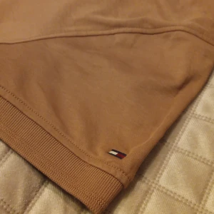 Brun pikétröja från Tommy Hilfiger - Stilig pikétröja från Tommy Hilfiger (Zipup).  Perfekt, passar bäst till stiliga. Alla endast 1 gång. Köpt för 79 dollar, från USA.