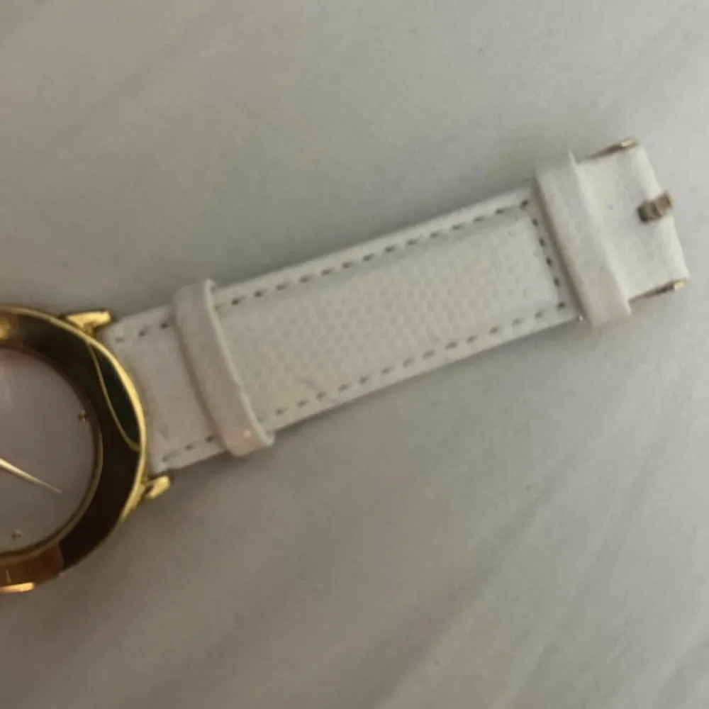 Elegant klocka från Aigner med vit läderrem och guldfärgad boett. Urtavlan är vit med subtila guldfärgade visare och Aigner-logotypen. Perfekt för den som söker en stilren och tidlös accessoar.. Asusteet.