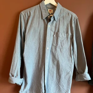 Blå skjorta från Levi's - Snygg blå skjorta från Levi's i storlek M. Skjortan har en klassisk krage och en bröstficka med en liten Levi's logga. Lite tjockare tyg som känns kvalitativt 