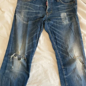 Blå jeans från Dsquared2 - Snygga blå jeans från Dsquared2 med slitna detaljer och en klassisk femficksdesign. De har en knappgylf och en röd etikett vid linningen. Perfekta för en avslappnad stil med en touch av edge.